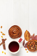 Light wooden background with a cup, sweet buns and autumn leaves.