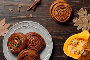 Pumpkin cinnabons, homemade seasonal pastries. Top view on a wooden background, with autumn leaves and a piece of pumpkin.