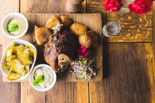 Top view of Golonka - oven-baked pork knuckle - traditional Polish dish served beautifully on a wooden board with oven-baked crispy potatoes, sauces, and pickles. High quality photo