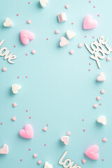 Valentine's Day concept. Top view vertical photo of inscriptions love heart shaped marshmallow candles and sprinkles on isolated pastel blue background with empty space in the middle