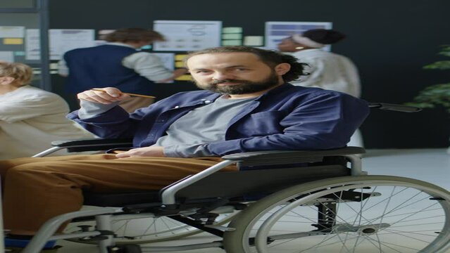 Vertical portrait shot of bearded businessman in wheelchair posing for camera at workplace in office