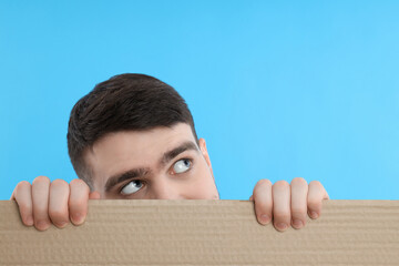 Half of man's face behind cardboard, look into something, on blue background