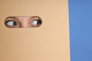 Hole in cardboard with young woman eyes