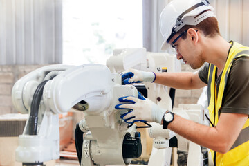 Professional caucsian male electronics engineer in gloves and helmet working in factory, welding robot inspecting electrical system structure. Safety industrial robotic arm wiring material.