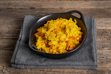 Black rustic plate with a portion of meat paella, on old wooden background, close-up.