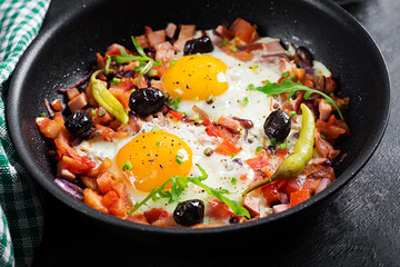 Fried eggs with vegetables on pan - pepperoni, tomatoes, ham, onion and black olives. Ketogenic breakfast.