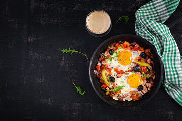 Fried eggs with vegetables on pan - pepperoni, tomatoes, ham, onion and black olives. Ketogenic breakfast. Top view, above