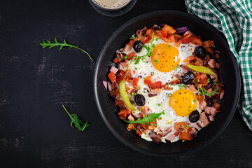 Fried eggs with vegetables on pan - pepperoni, tomatoes, ham, onion and black olives. Ketogenic breakfast. Top view, above