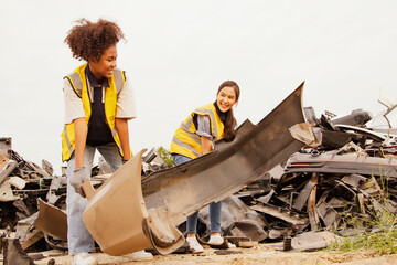Two cheerful female workers working in an outdoor warehouse collecting old broken pieces of old car...