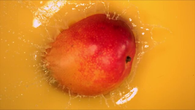 Super Slow Motion Shot of Mango Falling and Splashing into Juice on Yellow Background at 1000fps.
