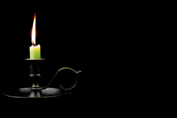 Burning candle in a old brass chamberstick candle holder isolated on black background with copy space