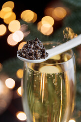 Black caviar in a mother-of-pearl spoon and glass of champagne with bokeh