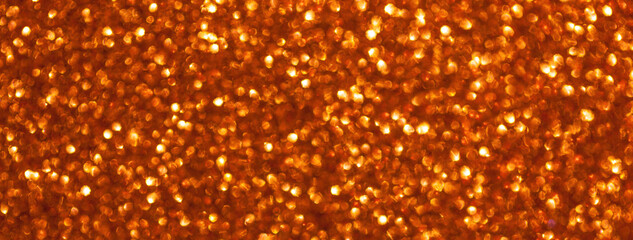 Blurred orange sparkling background from small sequins, macro. Shiny red glittery bokeh of christmas garland.