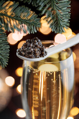 Black caviar in a mother-of-pearl spoon and glass of champagne with bokeh