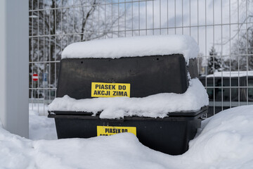 Plastic grit sand box bin for winter in Poland. Covered in snow on a cold day. Letters in Polish...