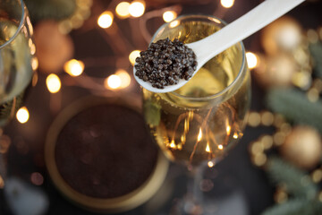 Black caviar in a mother-of-pearl spoon and glass of champagne with Christmas decoration - obrazy, fototapety, plakaty