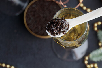 Black caviar in a mother-of-pearl spoon and glass of champagne with Christmas holiday decoration,...