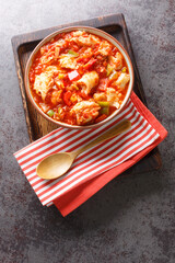Spanish style salted cod cooked with vegetables peppers, tomatoes, and onions close-up in a bowl on the table. Vertical top view from above
