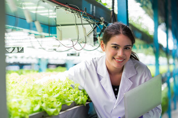 Young woman scientist holding laptop computer analyzes and studies research in organic, hydroponic...