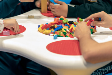 Group of crop children sitting at table and playing with colorful bricks on weekend day in playroom