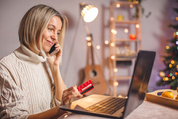 Smiling middle aged lady with laptop sitting at home and buying xmas gifts