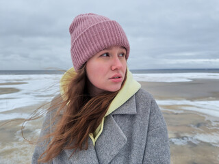 Portrait of young beautiful woman at winter cold day walking outdoors  in hat on the beach