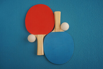 Red and blue table tennis or ping pong rackets and two balls lie on a blue background with a...