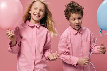 two happy cheerful children in pink shirts stand on a pink background and enjoy life with balloons in their hands