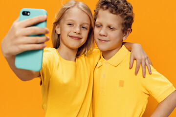 happy, cute children, brother and sister stand on a yellow background in bright clothes and take a...