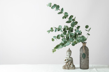 Modern minimal interior floral decoration with natural eucalyptus twig in vintage glass vase and Buddha statue