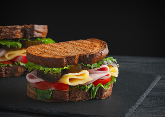 Delicious club sandwich with vegetables, ham, cheese and fried toast on a black background. Side view, copy space