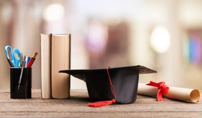 Graduation cap and stack of books on a table - obrazy, fototapety, plakaty