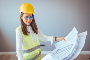 Portrait of woman engineer at building site looking at camera with copy space. Mature construction manager standing in yellow safety vest and blue hardhat with crossed arms. 