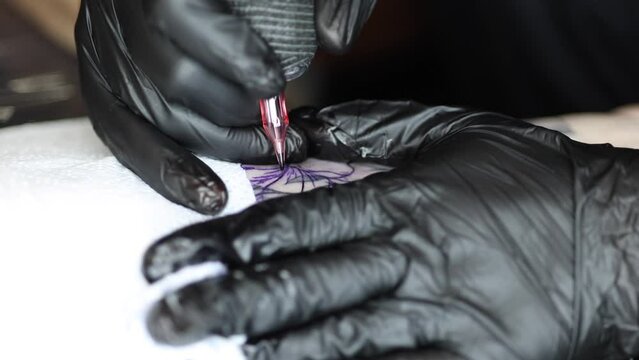 Close-up of a young professional tattoo artist introduces black ink into the skin using needle from a wireless tattoo machine. Tattoo on hand. Vertical video.