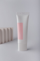 Cream tube with pink blank label, no brand mockup on white background with geometric concrete decor. Tender minimal composition