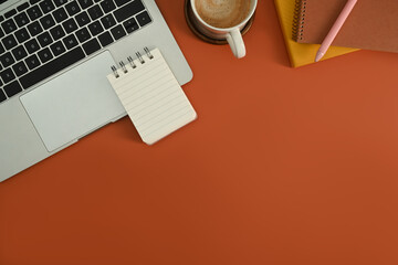 Laptop, notepad and cup of coffee on orange background. Flat lay, top view with copy space