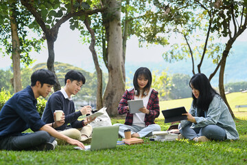 Young Asian college students working on group project and communicating while sitting on on campus lawn on beautiful day