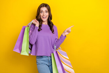 Photo of charming astonished girl hold bags indicate finger empty space proposition isolated on yellow color background