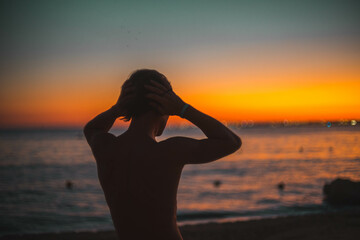 silhouette of a man with a naked torso at sunset by the sea. long haired man.