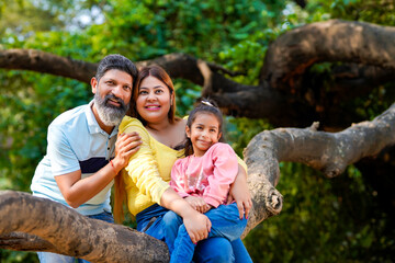 Happy indian couple sitting with his little girl on tree branch at garden.