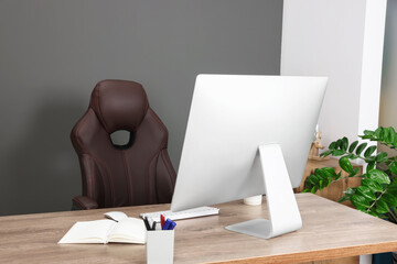 Computer, notebook and stationery on table near chair in office. Boss workplace