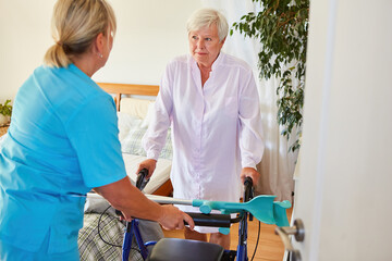 Krankenpflegerin hilft Seniorin mit Rollator beim Gehen