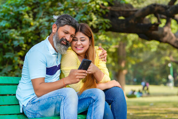 Indian man and woman watching some detail in smartphone at park.