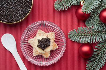 Black caviar appetizers bread star on a christmas decorated red background
