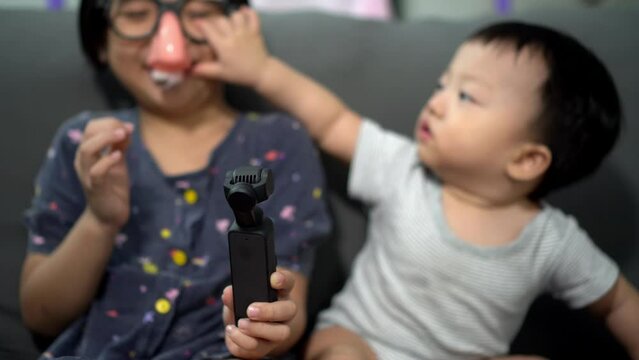 Naughty baby boy take the sister mask spectacle while selfie together with small gimbal camera.