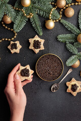 Black caviar appetizers stars in a human's hand on a christmas decorated black table