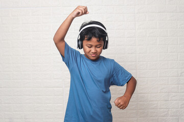 Young cute Asian boy wearing headphones listening to music and dancing isolated in white background