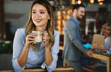 Portrait of happy young business woman drinking coffee in a break. In the background, her colleagues