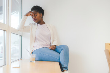 Beautiful sad afro female sitting alone at the cafe windowsill.Depressed woman at the city