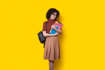 Curly-haired student woman with backpack holding some documents and books isolated over yellow background. Education in high school university